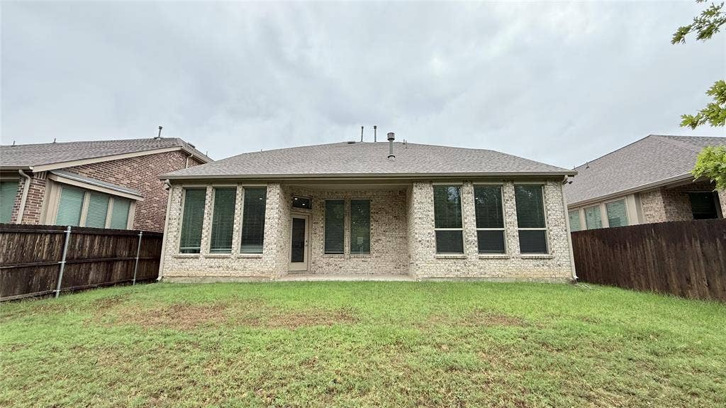 Expansive backyard with a manicured lawn, brick exterior, covered patio, and privacy fencing