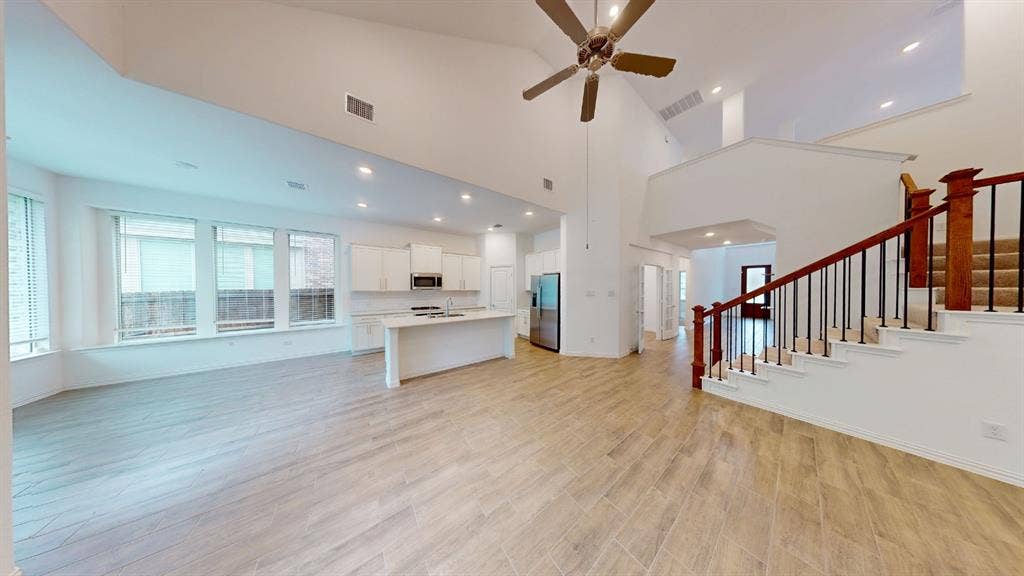 Open-concept living space featuring wood-finish flooring, a kitchen island with built-in cabinetry, stainless steel appliances, and high ceilings with a ceiling fan
