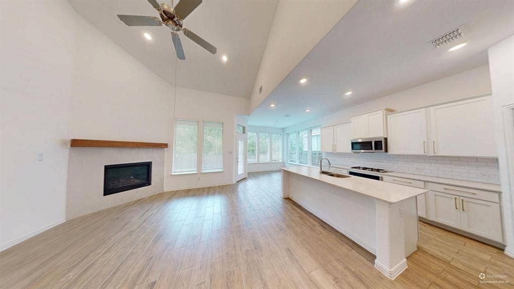 Vaulted ceilings with recessed lighting, integrated fireplace with a wood mantle, wood-finish flooring, white shaker cabinetry, and stainless steel appliances