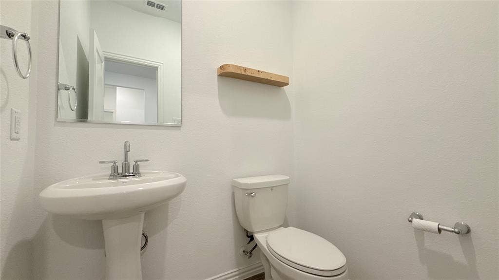 Pedestal sink with chrome faucet, wall-mounted mirror, white toilet, and wood shelf