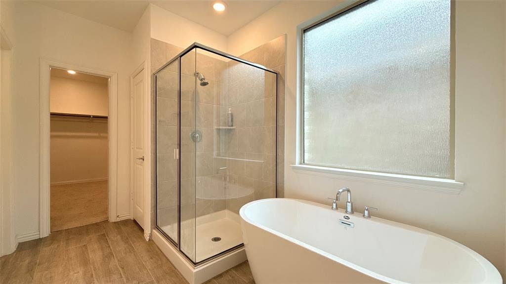 Freestanding soaking tub with chrome fixtures, glass-enclosed shower with tile surround, and wood-finish flooring