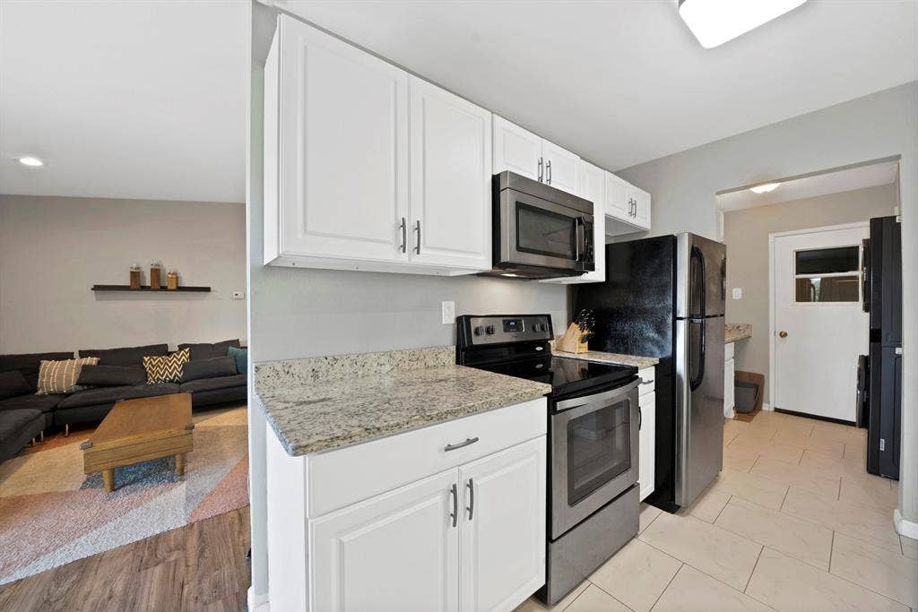 1400 Lorrie Drive, Richardson, TX 75080 Kitchen featuring appliances with stainless steel finishes, light stone counters, white cabinetry, open floor plan, and washer / clothes dryer