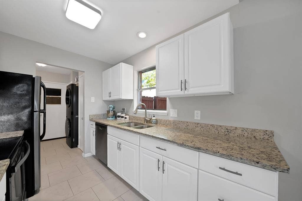 1400 Lorrie Drive, Richardson, TX 75080 Kitchen featuring light stone counters, white cabinetry, stacked washing machine and dryer, dishwashing machine, and light tile patterned flooring