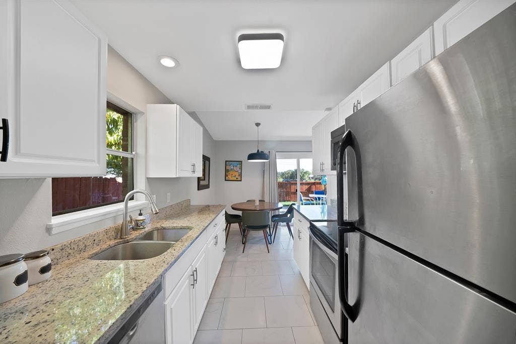 1400 Lorrie Drive, Richardson, TX 75080 Kitchen with stainless steel appliances, light stone counters, white cabinets, hanging light fixtures, and light tile patterned floors