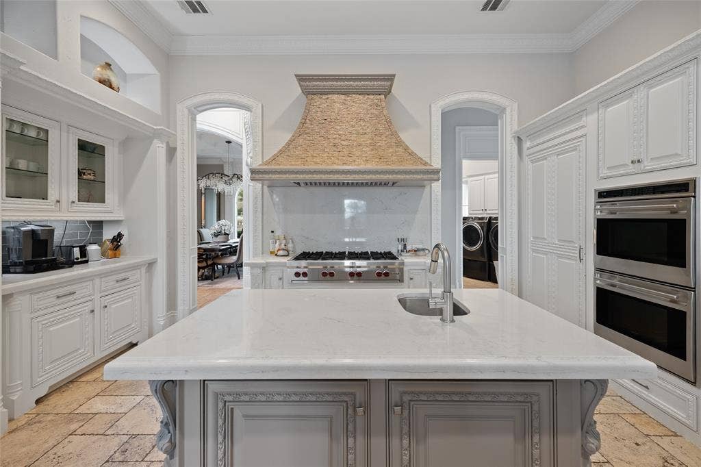 6300 Caroline Drive, Frisco, TX 75034 Central island with integrated sink, stone countertops, custom range hood, built-in double ovens, and decorative cabinetry