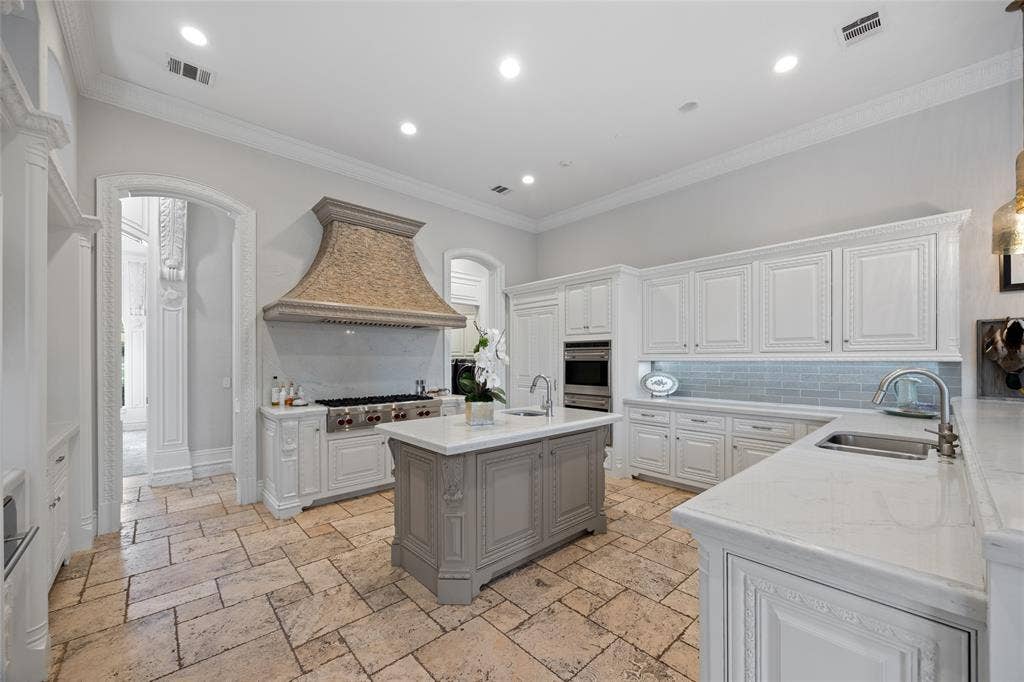 6300 Caroline Drive, Frisco, TX 75034 Kitchen featuring an oversized range hood, stainless steel appliances, a large center island, extensive cabinetry, and stone flooring