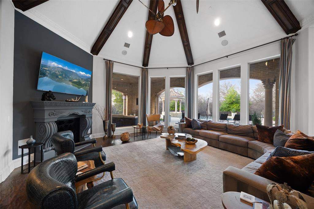 6300 Caroline Drive, Frisco, TX 75034 Vaulted ceiling with exposed wood beams, ornate fireplace with mantel, dark wood-finish flooring, and multiple large windows