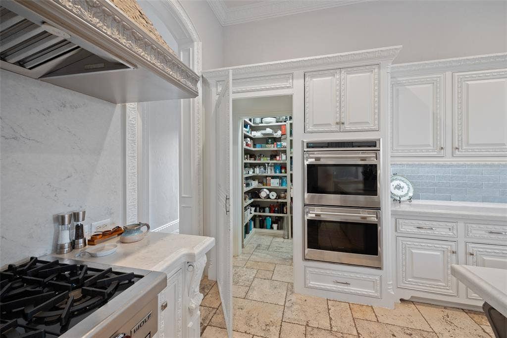6300 Caroline Drive, Frisco, TX 75034 White cabinetry with decorative molding, stainless steel double ovens, tile backsplash, and a walk-in pantry