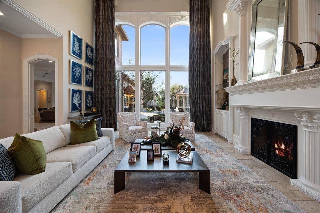 6300 Caroline Drive, Frisco, TX 75034 Two-story living area with full-height windows, ornate fireplace with custom mantel, built-in cabinetry, arched doorways, and tile flooring