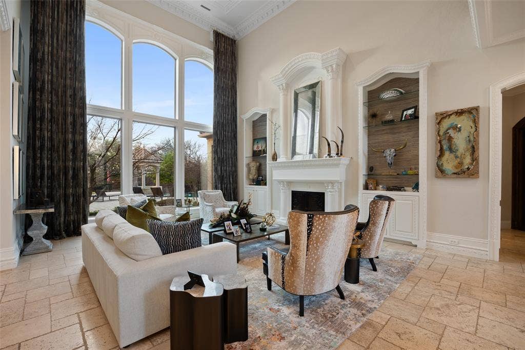6300 Caroline Drive, Frisco, TX 75034 Soaring ceilings with decorative crown molding, full-height arched windows, a stone fireplace with ornate mantel, and built-in shelving with glass fronts