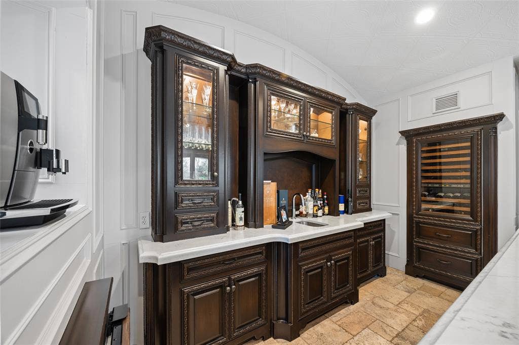 6300 Caroline Drive, Frisco, TX 75034 Built-in cabinetry with ornate detailing, glass-front upper cabinets with interior lighting, a built-in beverage refrigerator, a countertop with an integrated sink, and textured flooring