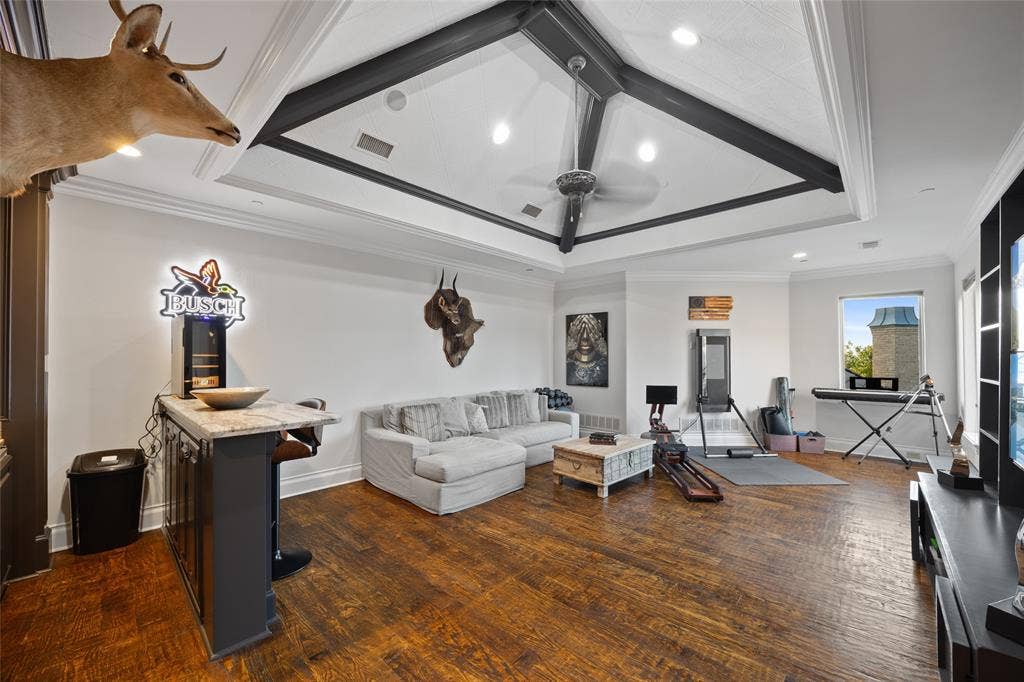 6300 Caroline Drive, Frisco, TX 75034 Spacious room featuring wood-finish flooring, a built-in wet bar with a stone countertop, a tray ceiling with exposed beams, and a ceiling fan