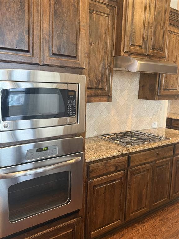 13721 Vera Cruz Road, Frisco, TX 75035 Built-in stainless steel microwave and oven, gas cooktop, granite countertops, wood cabinetry, and diamond-patterned tile backsplash