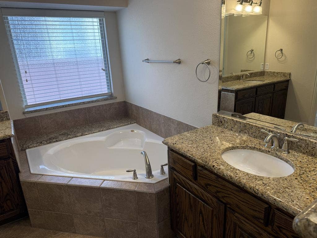 13721 Vera Cruz Road, Frisco, TX 75035 Deep soaking tub, dual vanity with undermount sinks, granite countertops, wood-finish cabinetry, and tiled tub surround