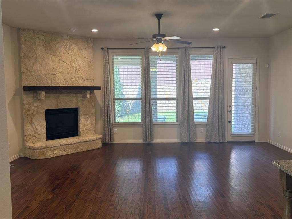 13721 Vera Cruz Road, Frisco, TX 75035 Stone-clad fireplace with a wood mantel, dark wood-finish flooring, recessed lighting, and a ceiling fan
