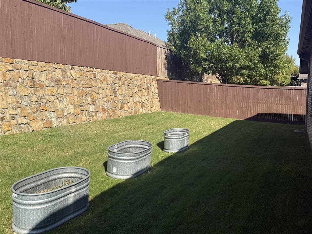 13721 Vera Cruz Road, Frisco, TX 75035 Expansive lawn area featuring a stone retaining wall and a wood privacy fence