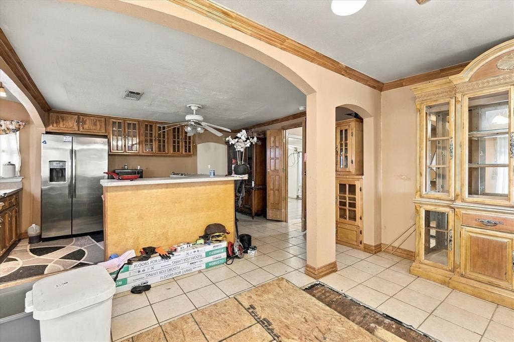 Kitchen featuring wood cabinetry, stainless steel refrigerator, breakfast bar with solid surface countertop, arched entryways, and built-in glass-front display hutch