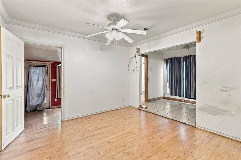Interior space featuring wood-finish flooring, a ceiling fan with integrated light fixture, crown molding, and tiled flooring in the secondary area