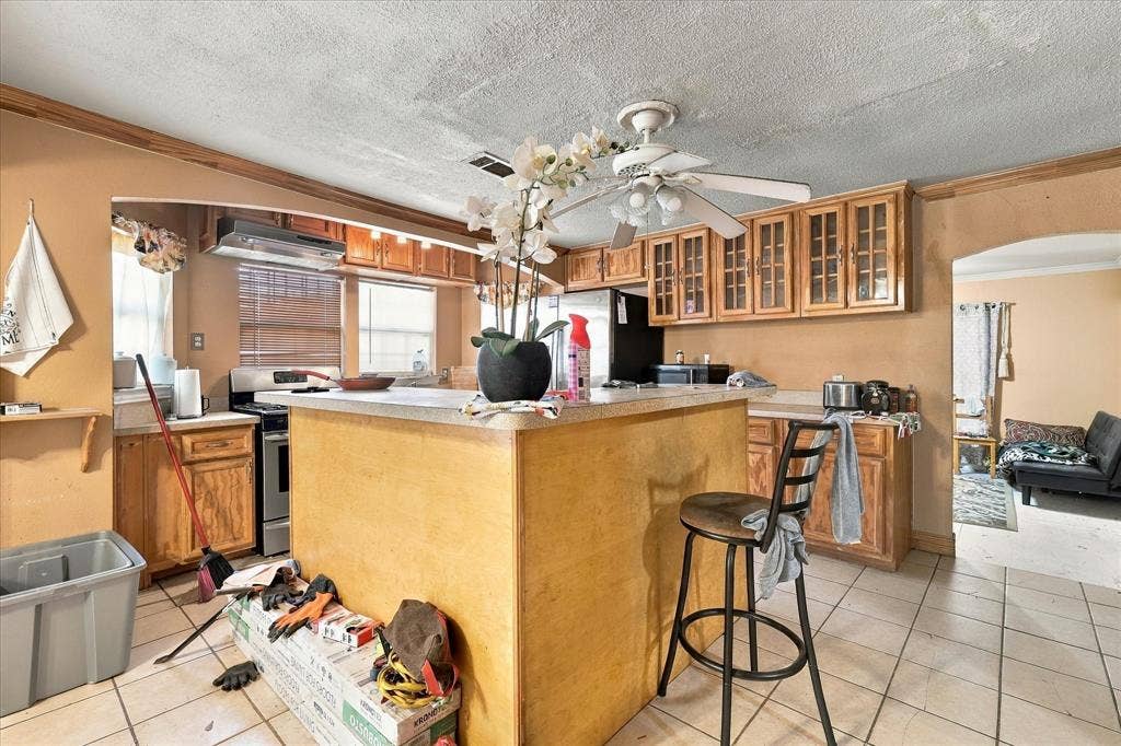 Kitchen featuring an island with a laminate countertop, wood cabinetry, tile flooring, an integrated range hood, and a ceiling fan with light fixture