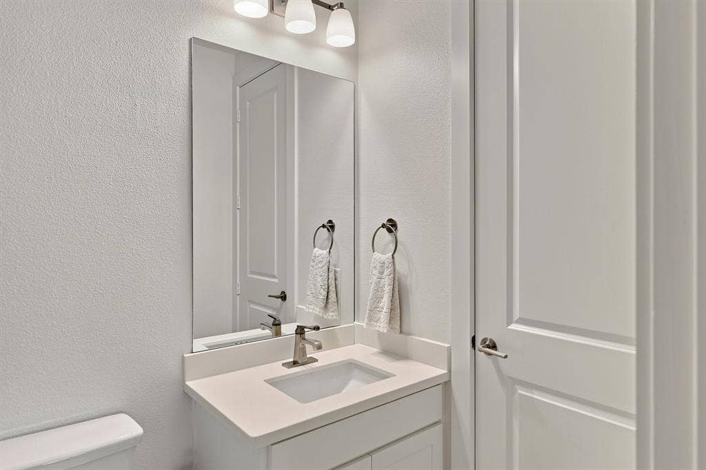 1137 Manderly Court, Dallas, TX 75204 White shaker-style vanity with an integrated sink and light-toned countertop, complemented by a wall-mounted mirror and brushed nickel fixtures