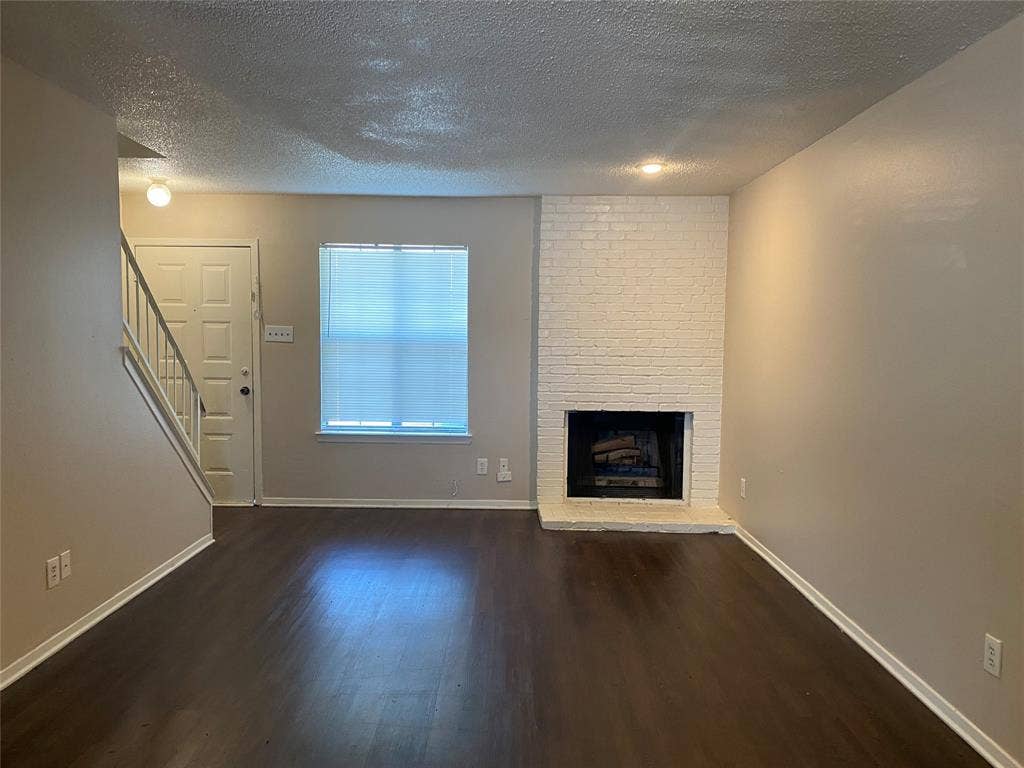 2802 Wimbledon Court, #B, Garland, TX 75041 Unfurnished living room with stairway, a fireplace, baseboards, a textured ceiling, and wood finished floors