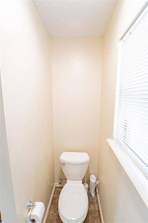 White toilet with a standard flush mechanism, complemented by a window featuring white blinds