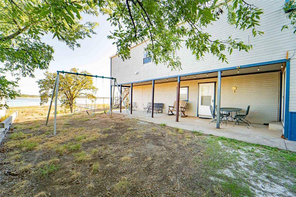 Expansive waterfront property featuring a covered patio, exterior staircase, and mature trees