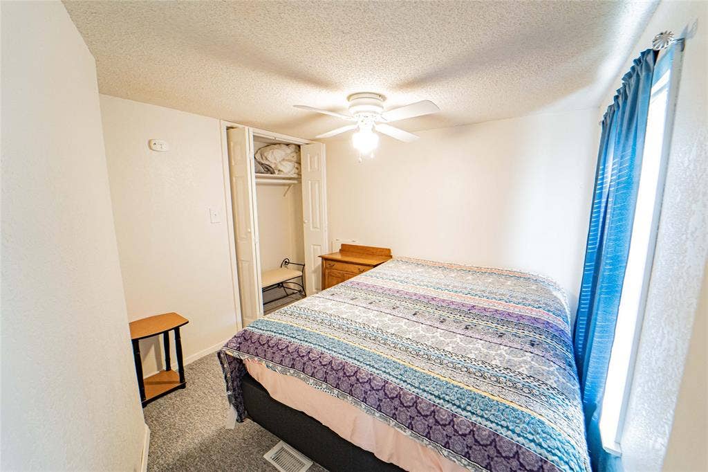 White walls, textured ceiling, ceiling fan with light fixture, carpeted flooring, and a window