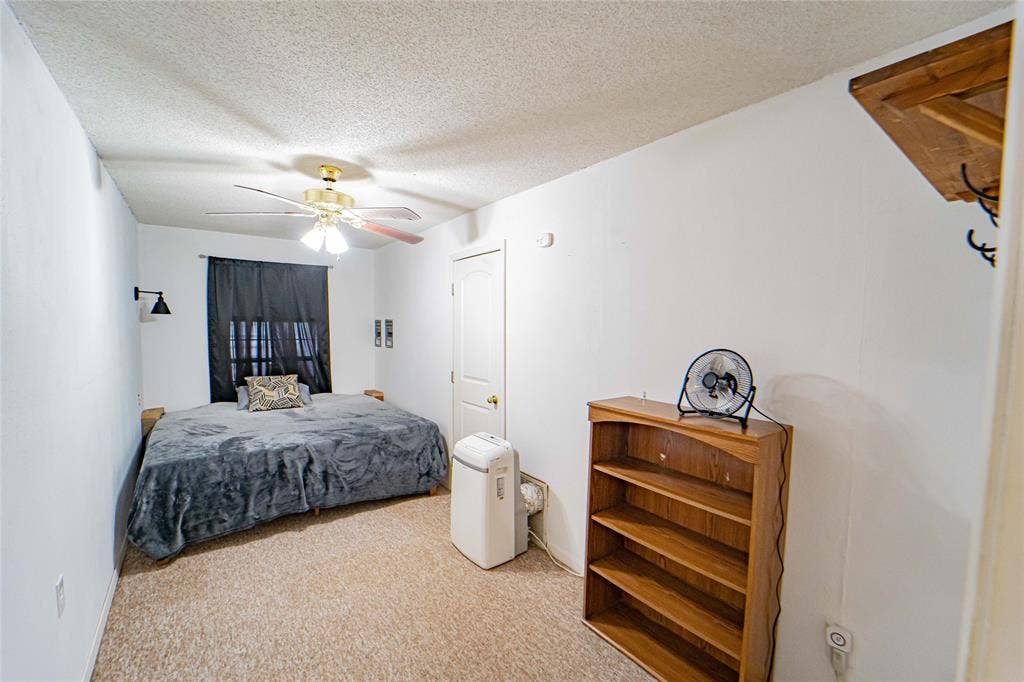 Carpeted room with a ceiling fan, sconce lighting, and white walls.