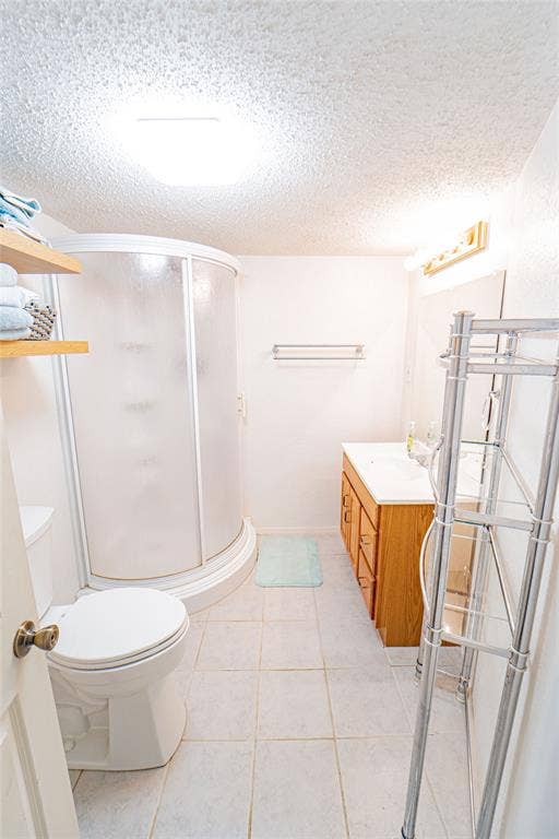 White tiled flooring, a white toilet, and a curved glass shower enclosure