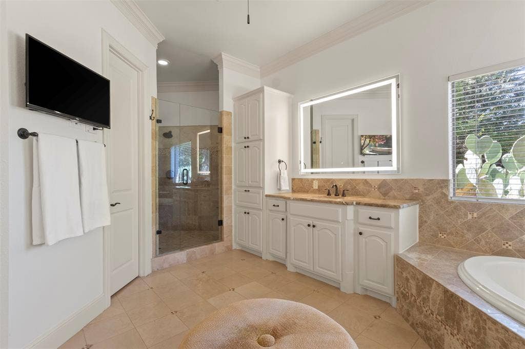 15600 Big Horn Trail, Frisco, TX 75035 Tile flooring, white vanity with integrated sink, freestanding soaking tub, glass-enclosed shower, and built-in storage cabinetry
