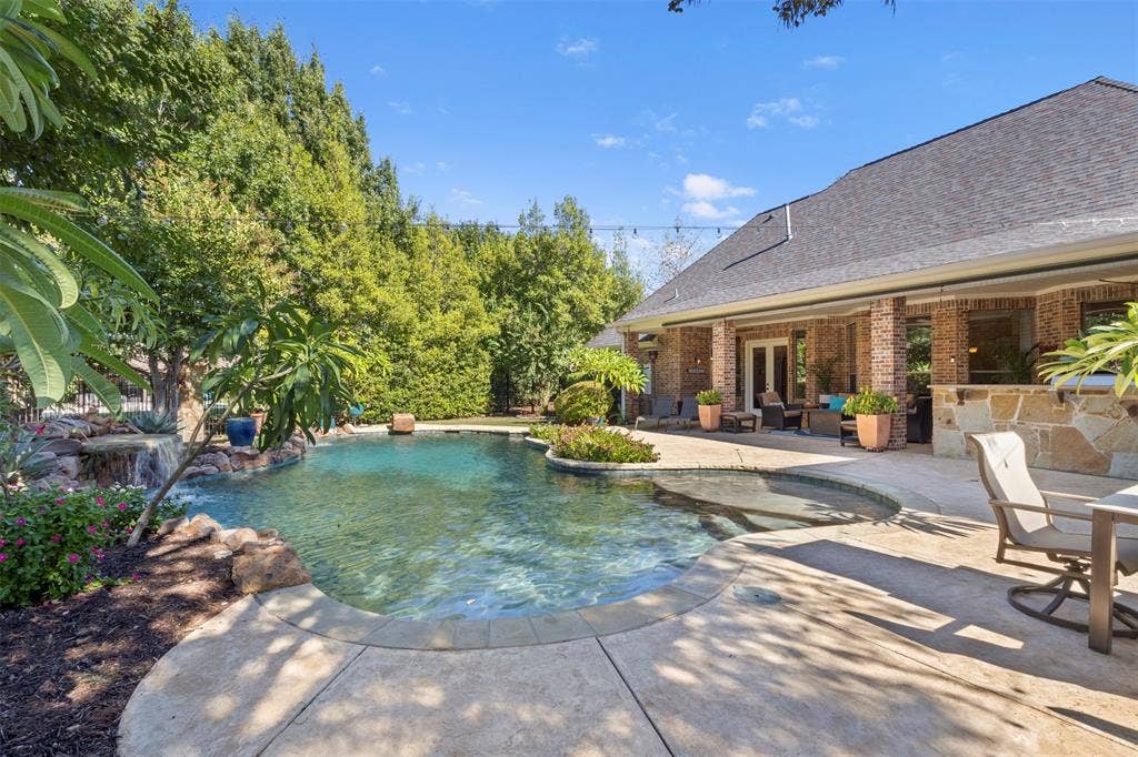 15600 Big Horn Trail, Frisco, TX 75035 Expansive backyard featuring a custom pool with a rock waterfall, a built-in spa, a large concrete patio, and a covered porch with brick columns