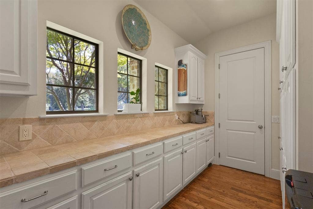 15600 Big Horn Trail, Frisco, TX 75035 White cabinetry, tile countertops, tile backsplash, wood-finish flooring, and multiple windows
