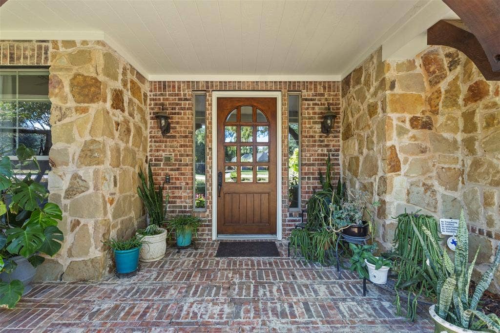 15600 Big Horn Trail, Frisco, TX 75035 Arched wood-panel entry door, brick-patterned flooring, stone and brick exterior accents, and dual exterior light fixtures