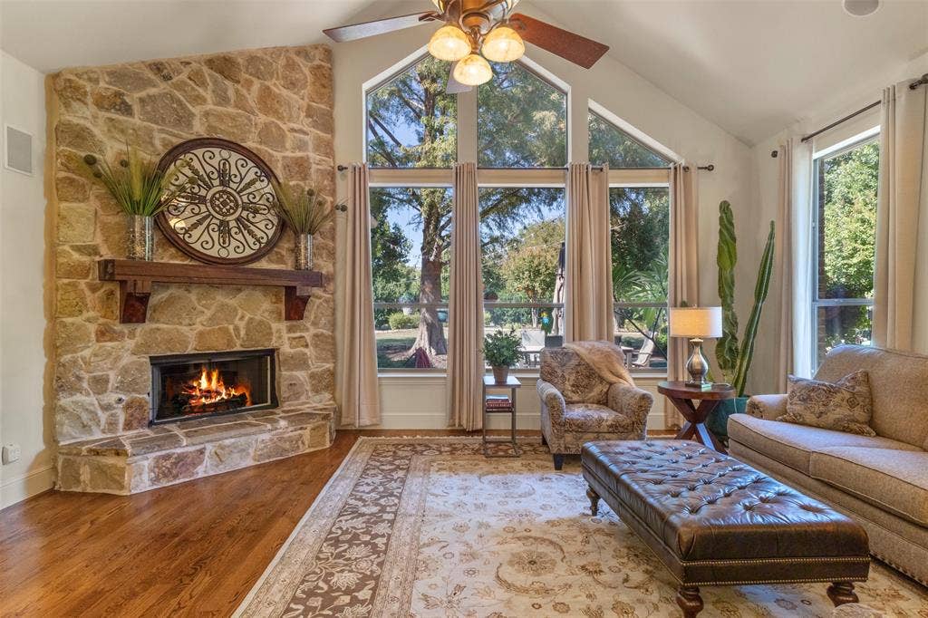 15600 Big Horn Trail, Frisco, TX 75035 Stone-clad fireplace with wood mantel, vaulted ceiling, wood-finish flooring, and expansive windows