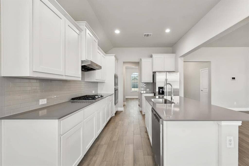3636 Wintergreen Street, Grand Prairie, TX 76065 Modern kitchen featuring white cabinetry, gas cooktop, stainless steel appliances, quartz countertops, subway tile backsplash, and wood-finish flooring throughout the open layout with an island workspace