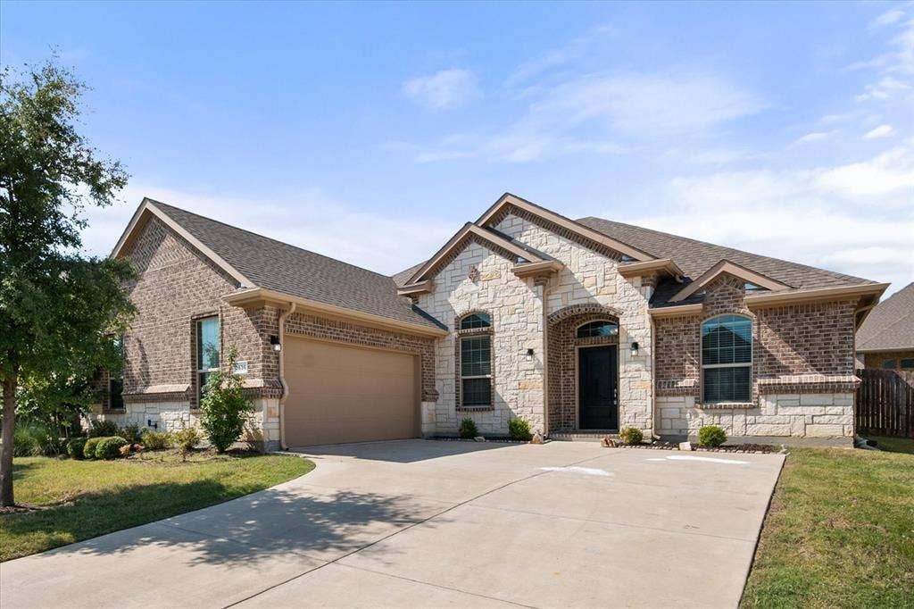 3636 Wintergreen Street, Grand Prairie, TX 76065 Brick and stone facade, arched entryway, attached garage, concrete driveway, and established landscaping