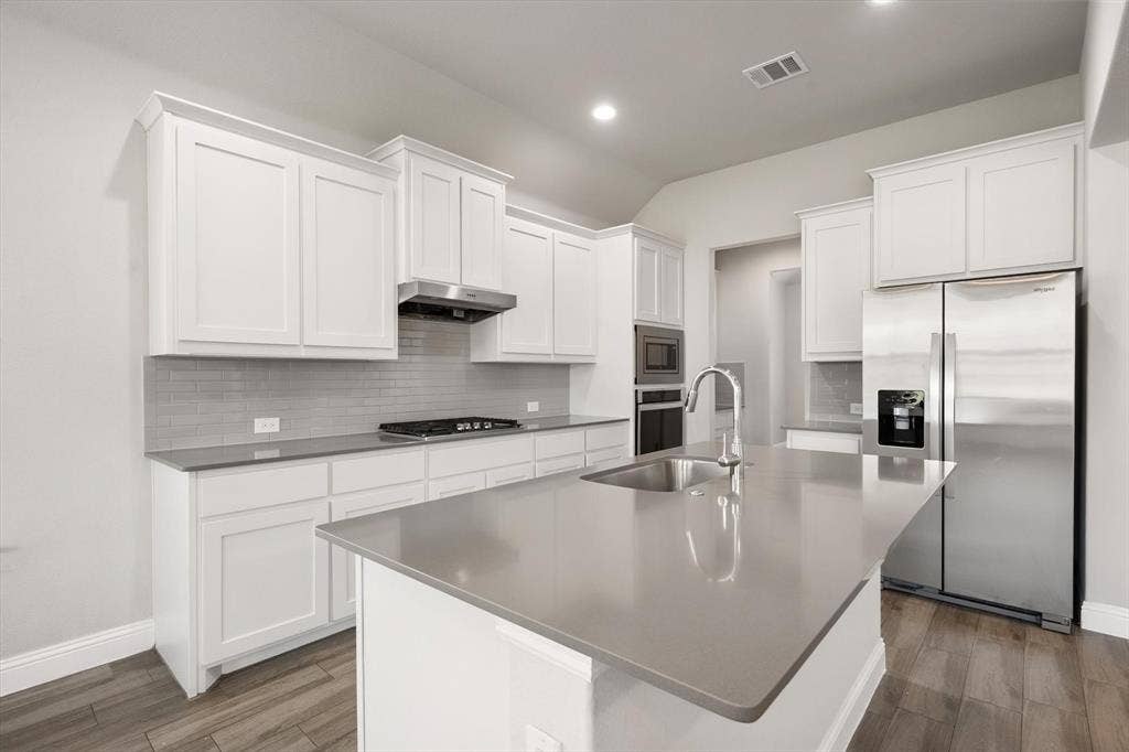 3636 Wintergreen Street, Grand Prairie, TX 76065 Contemporary kitchen featuring crisp white cabinetry, stainless steel appliances including a gas cooktop and built-in wall oven, quartz countertops, and a large island with extended seating