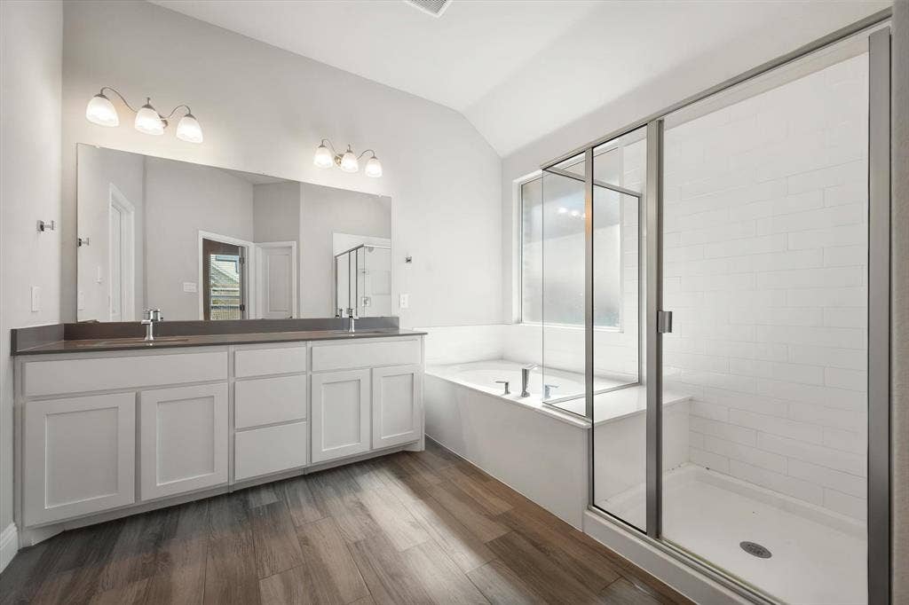 3636 Wintergreen Street, Grand Prairie, TX 76065 Wood-finish flooring, dual vanity with white cabinetry, built-in bathtub, glass-enclosed shower, and subway tile shower surround