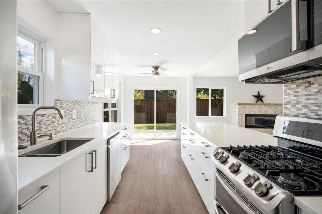 Kitchen featuring high-gloss white cabinetry, quartz countertops, stainless steel appliances, multi-toned tile backsplash, and wood-finish flooring