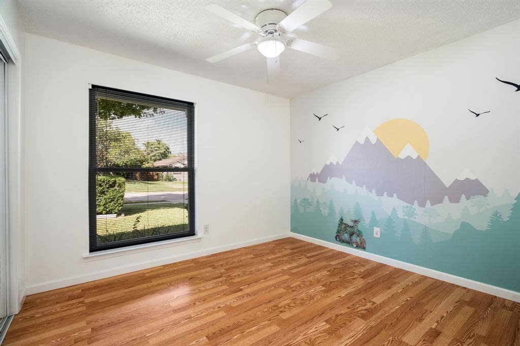 Wood-finish flooring, ceiling fan with integrated lighting, and a large window featuring horizontal blinds
