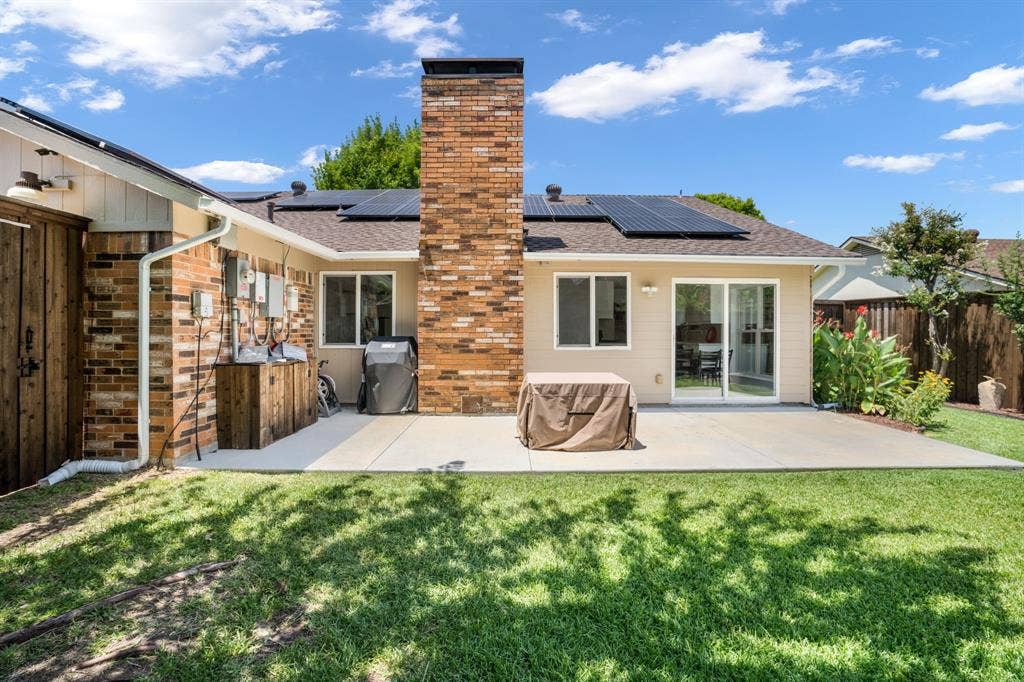 Backyard featuring a concrete patio, exterior brick chimney, roof-mounted solar panels, wood siding, and sliding glass doors