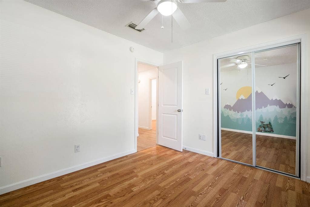 Wood-finish flooring, mirrored sliding closet doors, and a ceiling-mounted light fixture with a fan