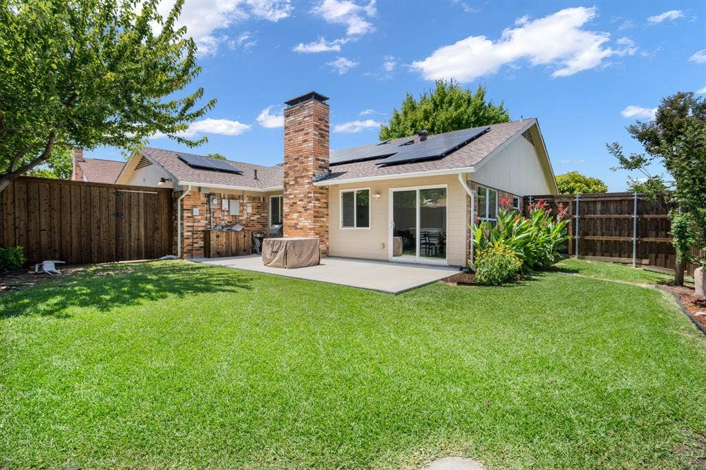 Rear exterior featuring a concrete patio, brick chimney, solar panels, and wood fencing