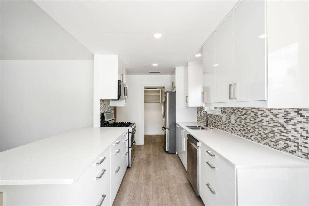 Kitchen featuring white high-gloss cabinetry, stone-surface countertops, multi-tonal mosaic tile backsplash, stainless steel appliances, and wood-finish flooring