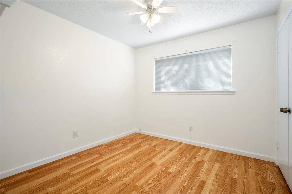 Room featuring wood-finish flooring, a white ceiling fan with integrated lighting, and a horizontal window with white blinds
