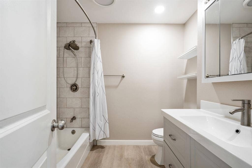 Tub and shower combination with subway tile surround, single vanity with integrated sink, wood-finish flooring, and recessed lighting