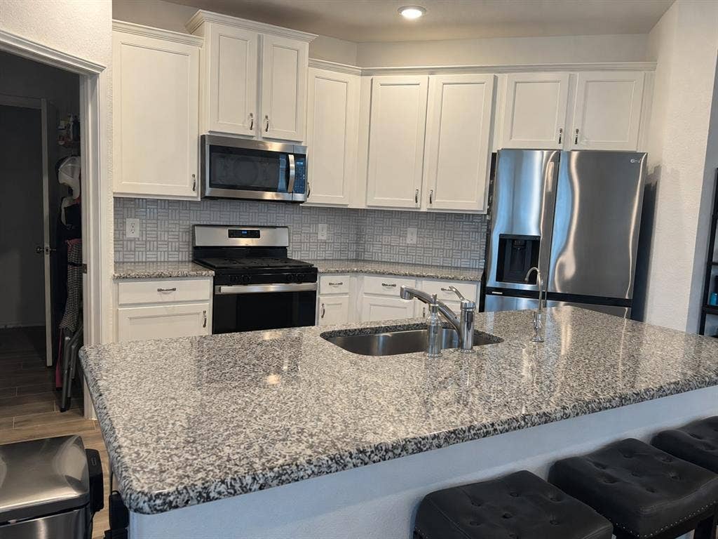 5719 Huffines Boulevard, Royse City, TX 75189 Kitchen featuring white cabinetry, stainless steel appliances, speckled stone countertops, and a tiled backsplash