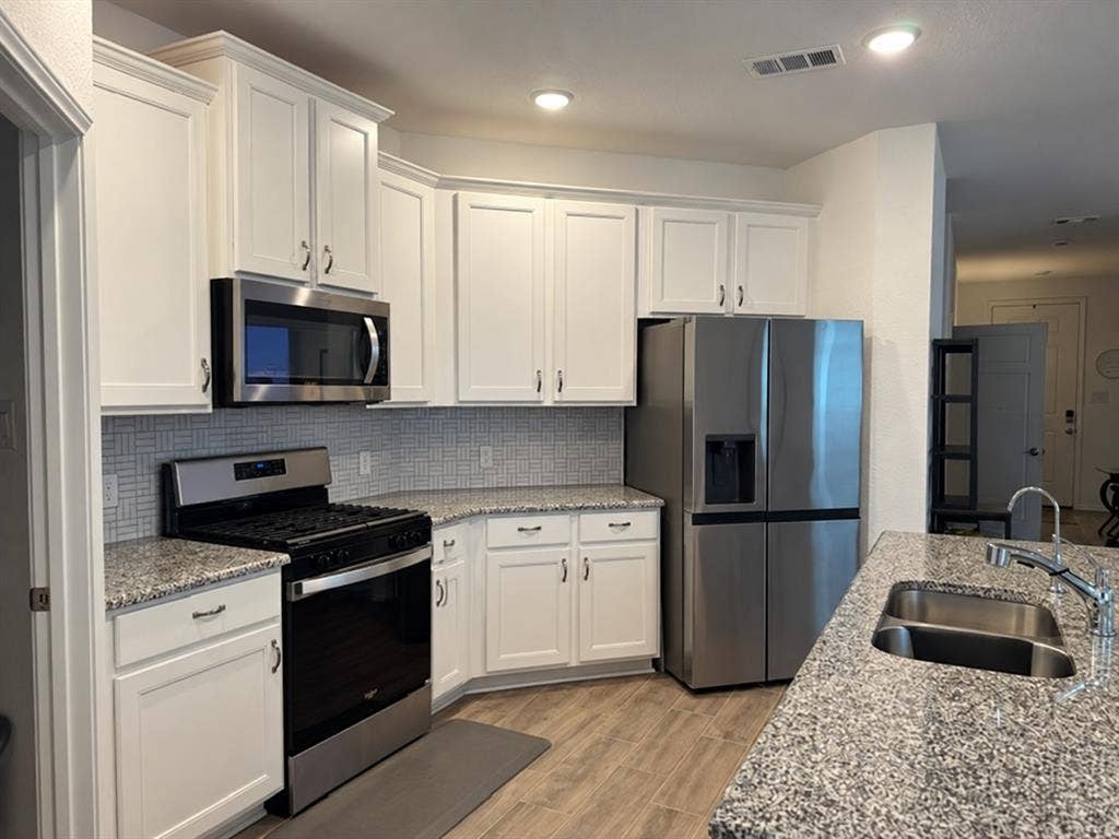 5719 Huffines Boulevard, Royse City, TX 75189 White cabinetry with crown molding, stainless steel appliances, granite-style countertops, mosaic tile backsplash, and wood-finish flooring