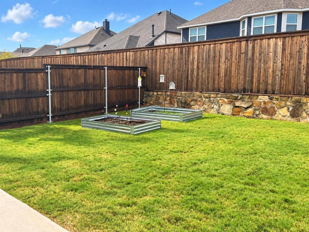 5719 Huffines Boulevard, Royse City, TX 75189 Expansive lawn area, wood privacy fencing, stone retaining wall, and two galvanized raised garden beds
